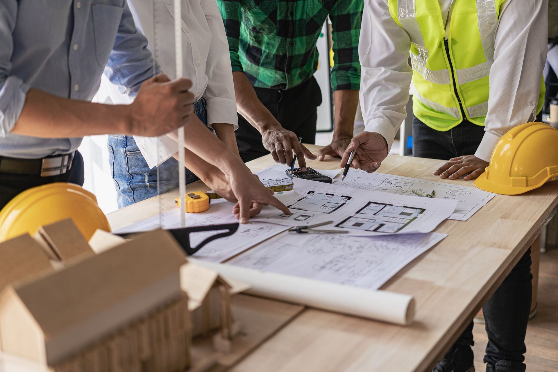 Workers reviewing blueprints at a construction site table with yellow hard hats and a rolled plan