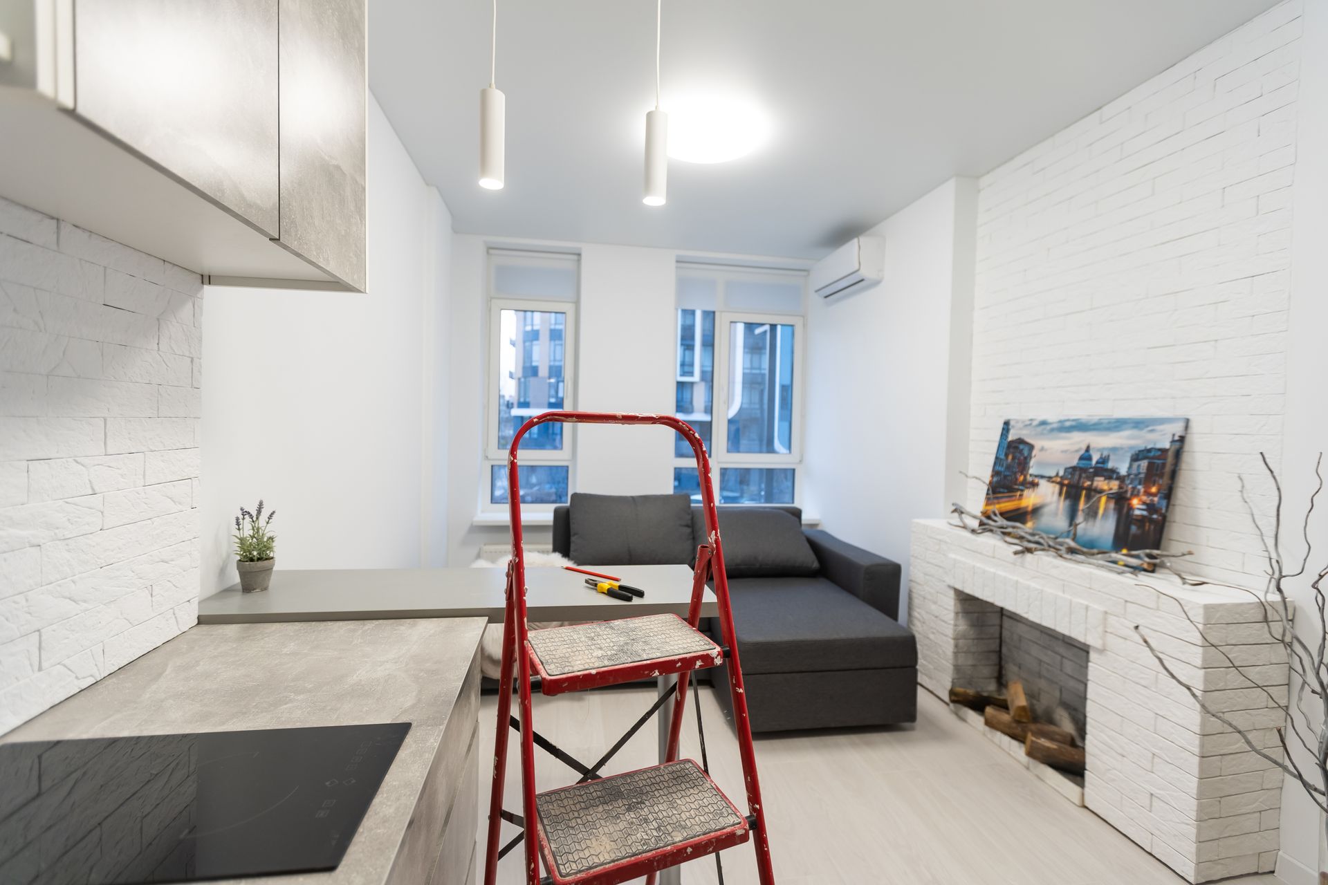 Bright modern kitchen and living area with a red step ladder, gray sofa, and fireplace.