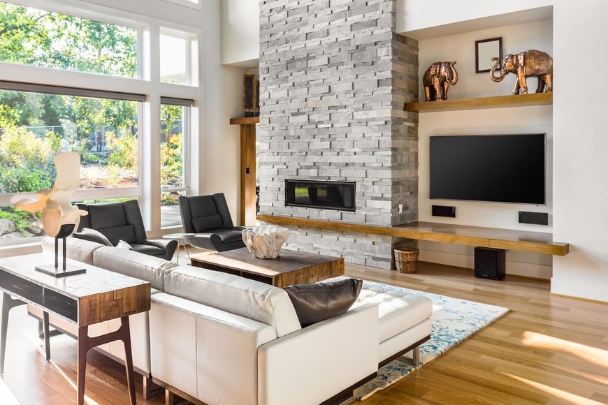 Bright modern living room with white sectional, stone fireplace, large windows, and built-in TV area