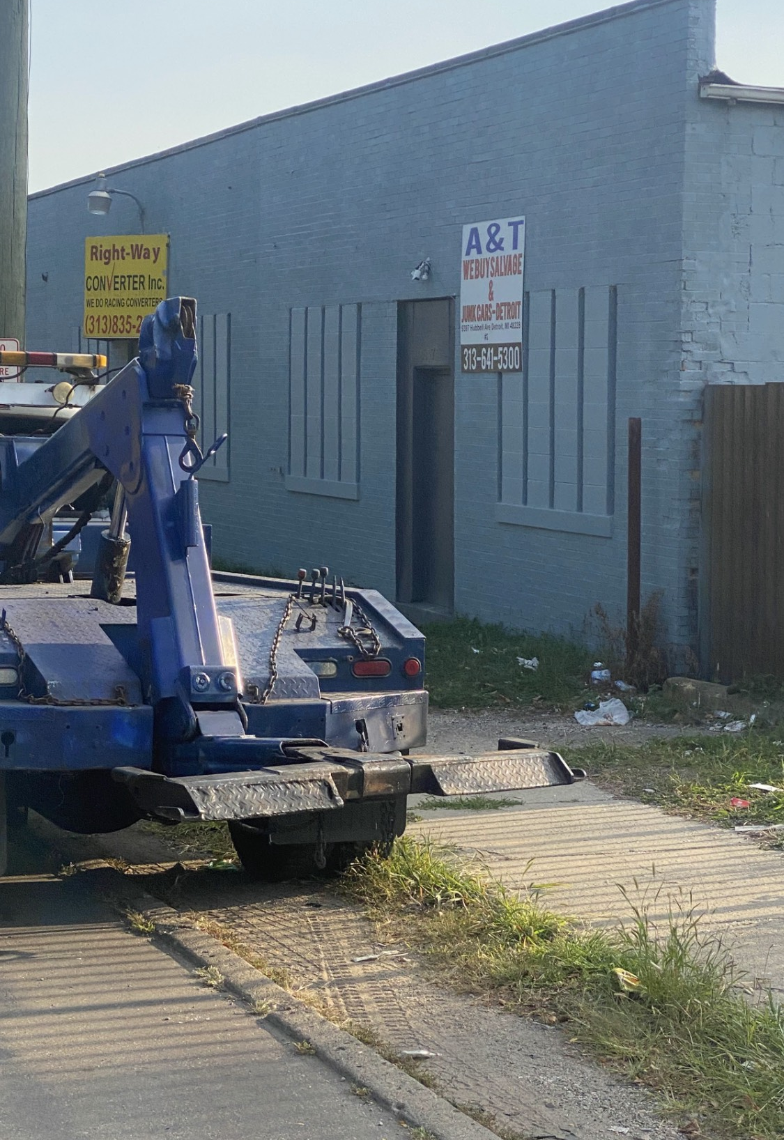 Blue tow truck in front of a blue building with a sign that reads 