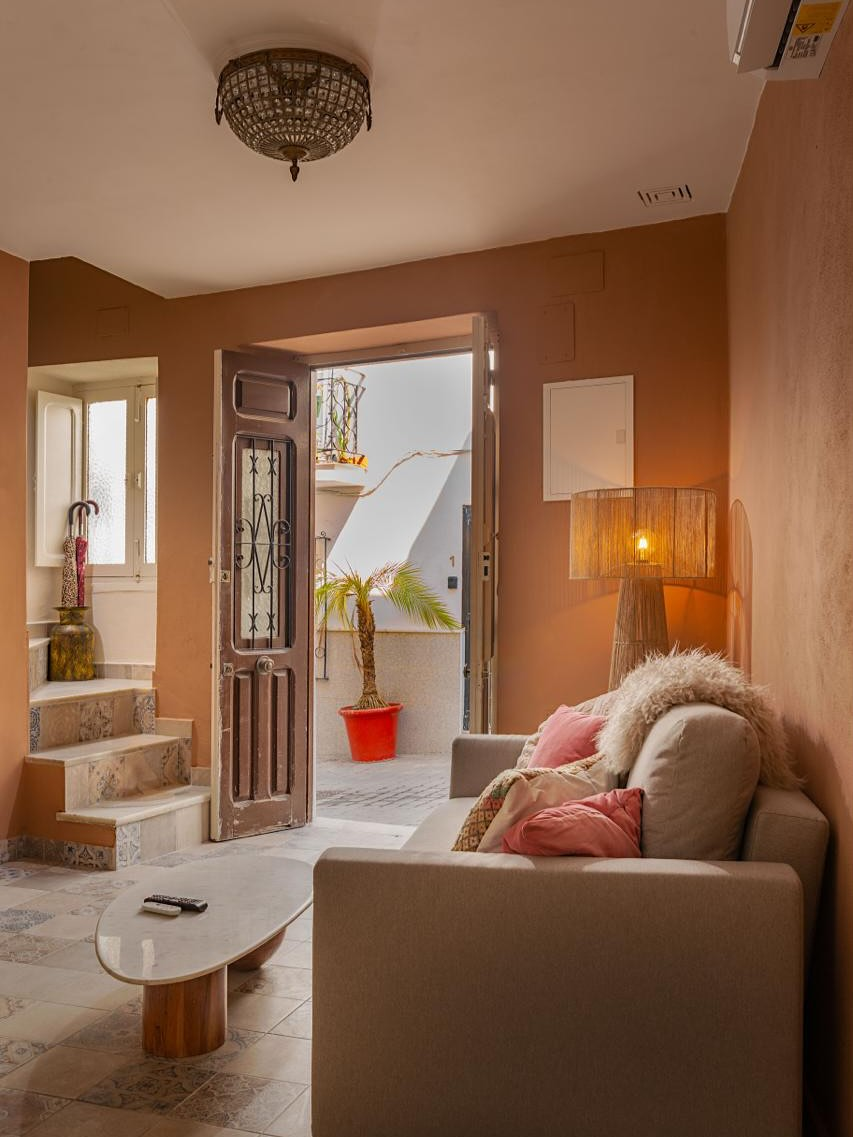 Woonkamer met beige bank, open deur naar de binnenplaats, terracotta muren.