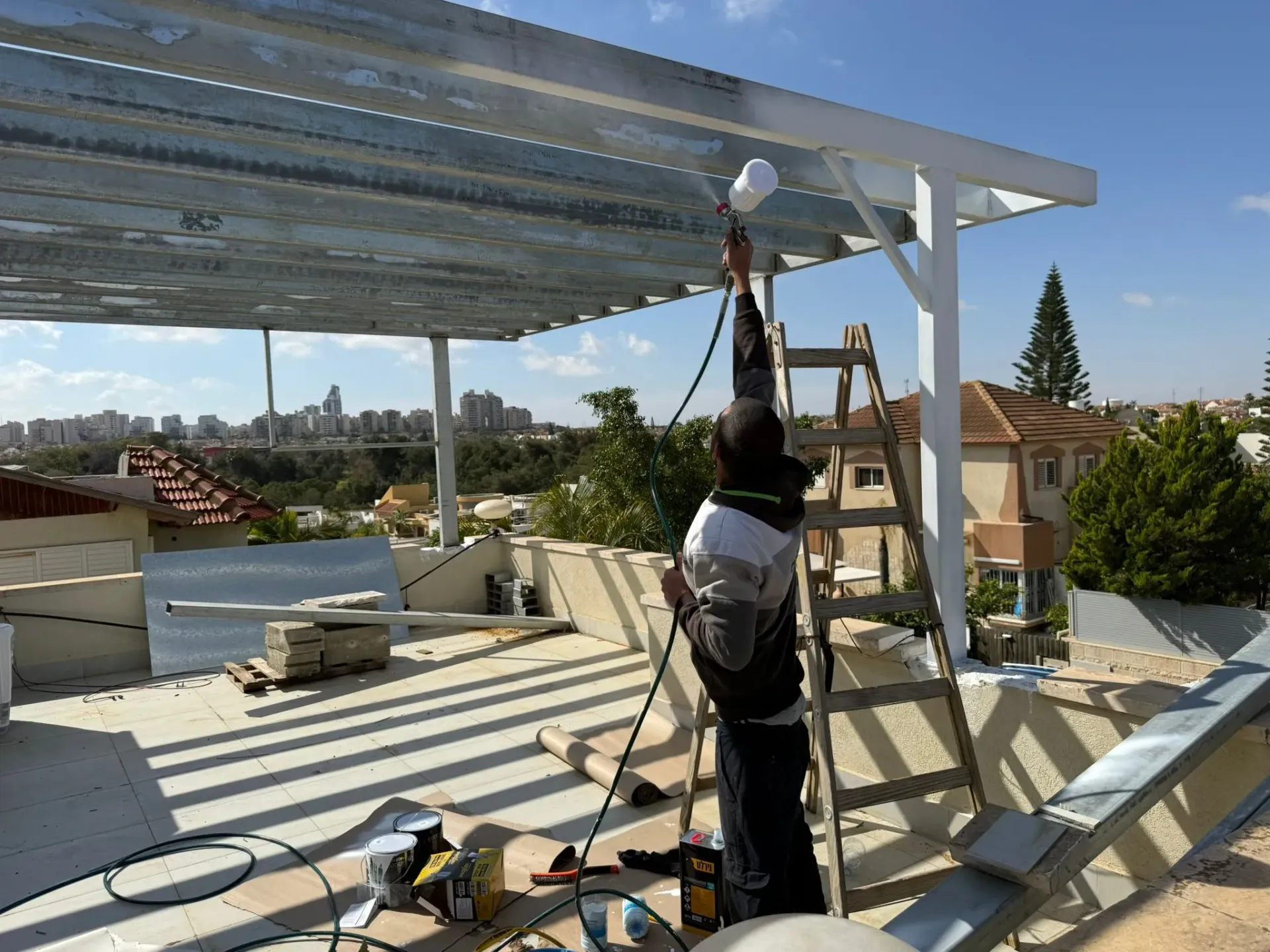 עובד על גג מתקין מסגרת פאנל סולארי לבן, עם כלים ונוף של העיר ברקע.