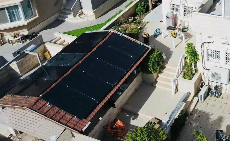 מבט אווירי על בית עם גג שחור ופטיו, שביל וגינון חצר מסביב