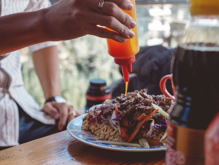 Sauce being squeezed over a plated meal at a restaurant table