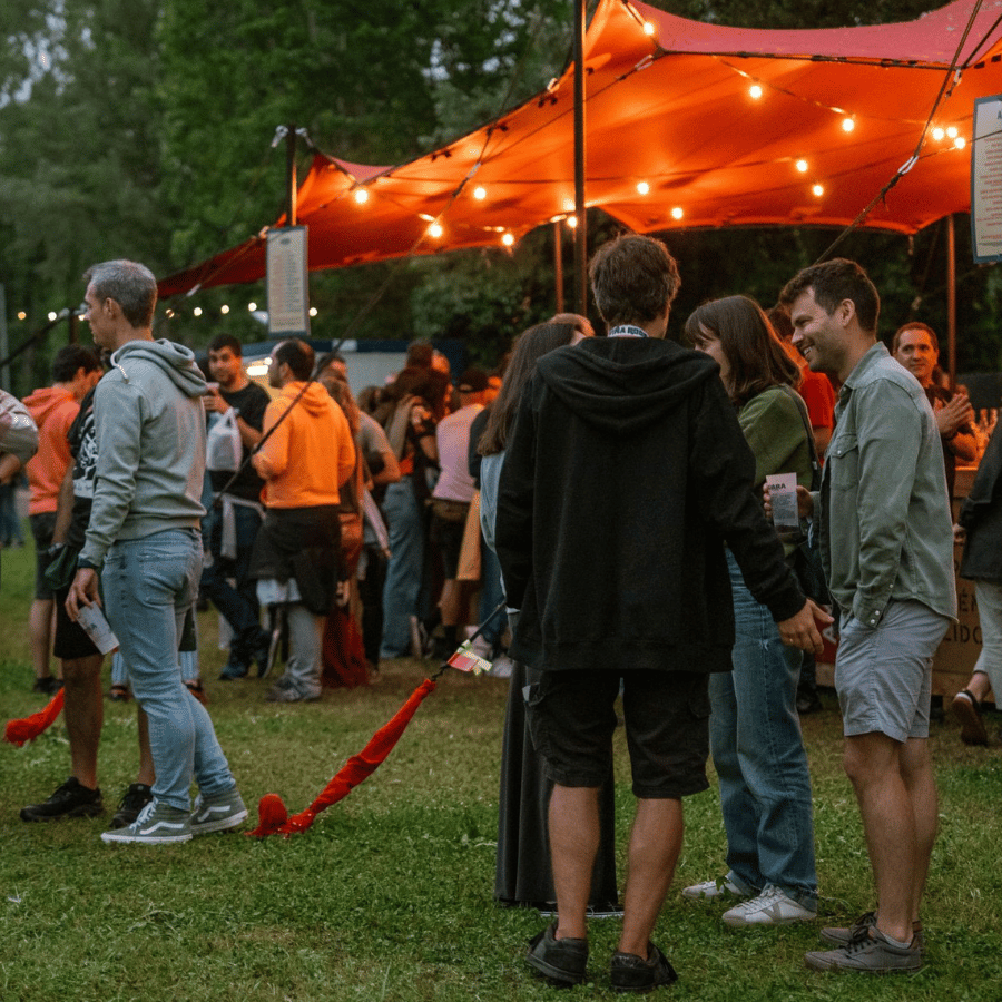 People gathered under orange canopy lights at an outdoor evening event.
