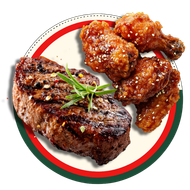 Grilled steak and glazed chicken wings on a white plate with red and green rim, garnished with herbs