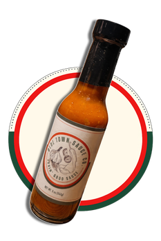 Amber hot sauce bottle with black cap, tilted over a red-and-green circular label background