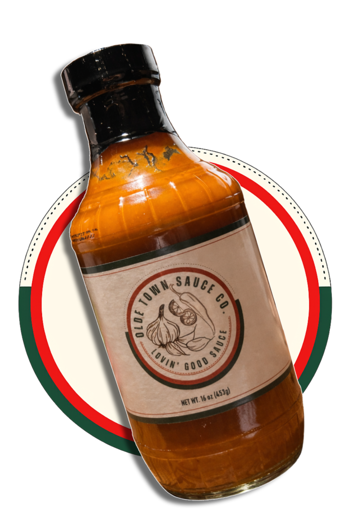 Tilted amber sauce bottle with black cap and cream label on a red-and-green circle background