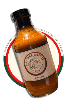 Tilted amber sauce bottle with black cap and cream label on a red-and-green circle background
