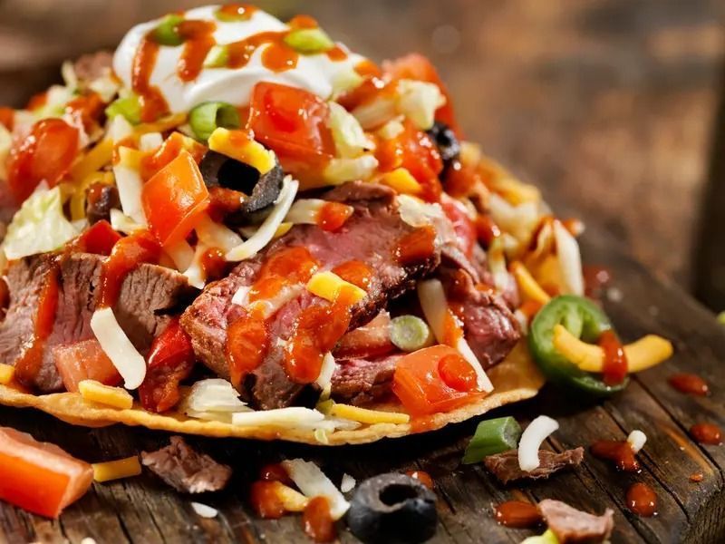 Loaded nachos topped with melted cheese, tomatoes, olives, jalapeños, and sour cream on a platter