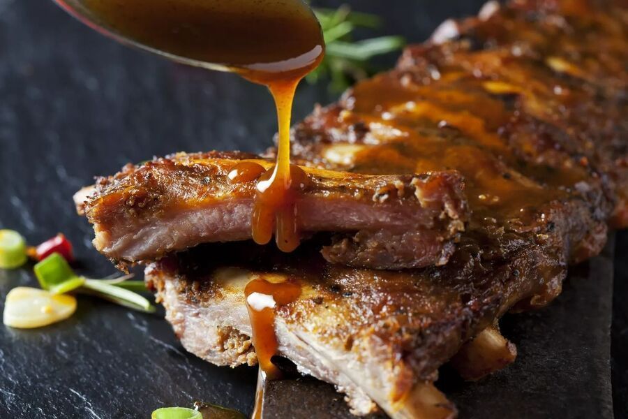 Barbecue ribs being basted with sauce on a plate, with vegetables in the background