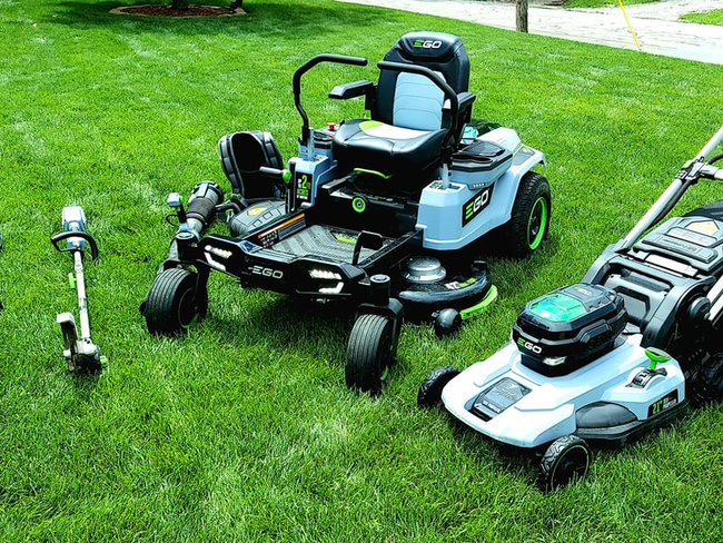 A lawn mower , trimmer , and a tractor are sitting on top of a lush green lawn. A lawn mower , trimmer , and a tractor are sitting on top of a lush green lawn.