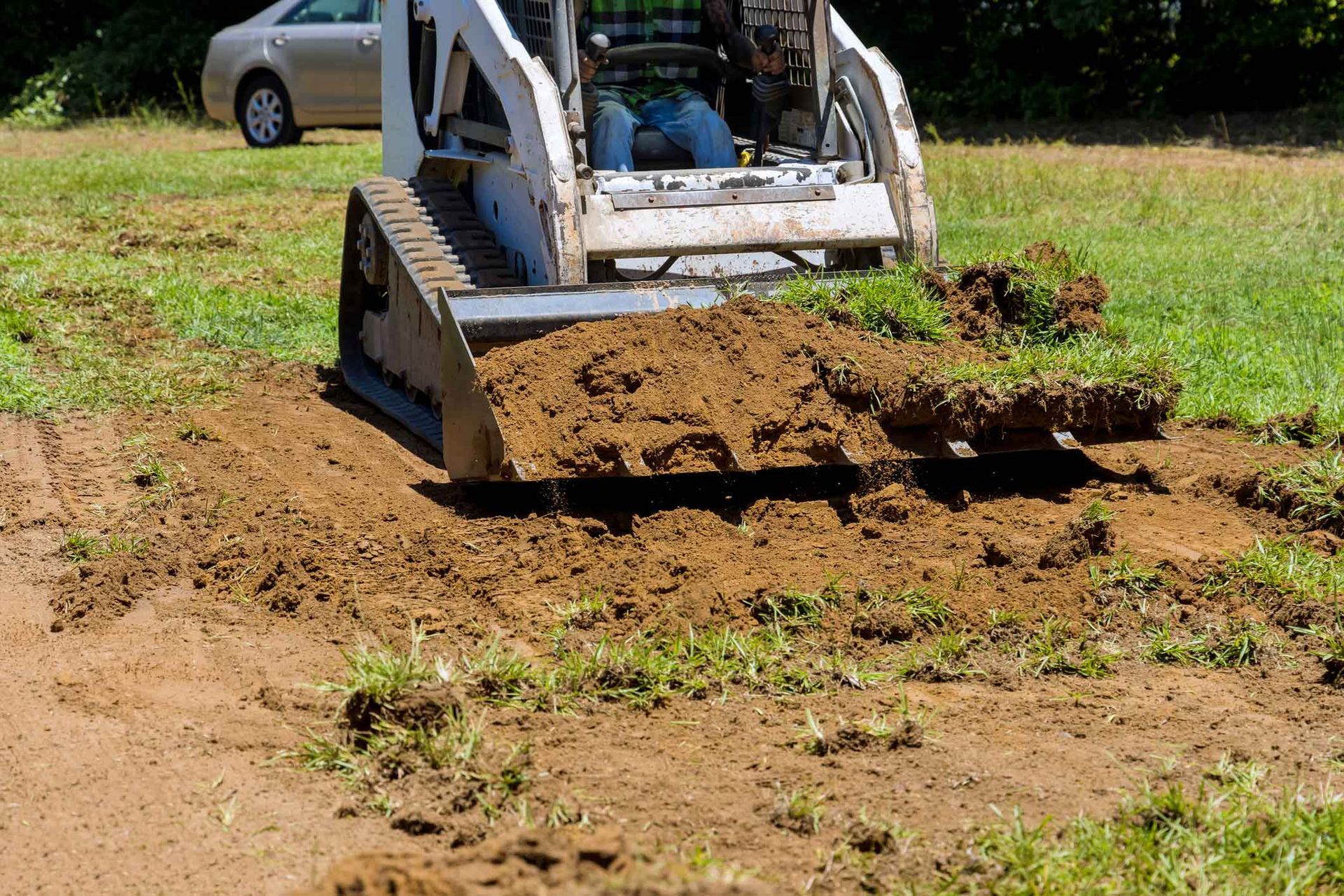 Bobcat scooping up dirt and grass on a grassy area, preparing the ground.
