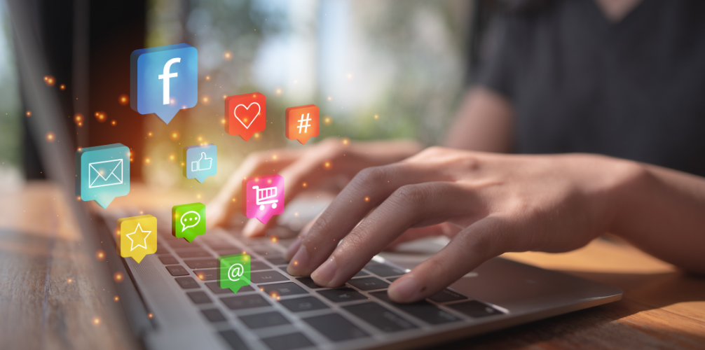 A person is typing on a laptop computer with social media icons coming out of the screen.