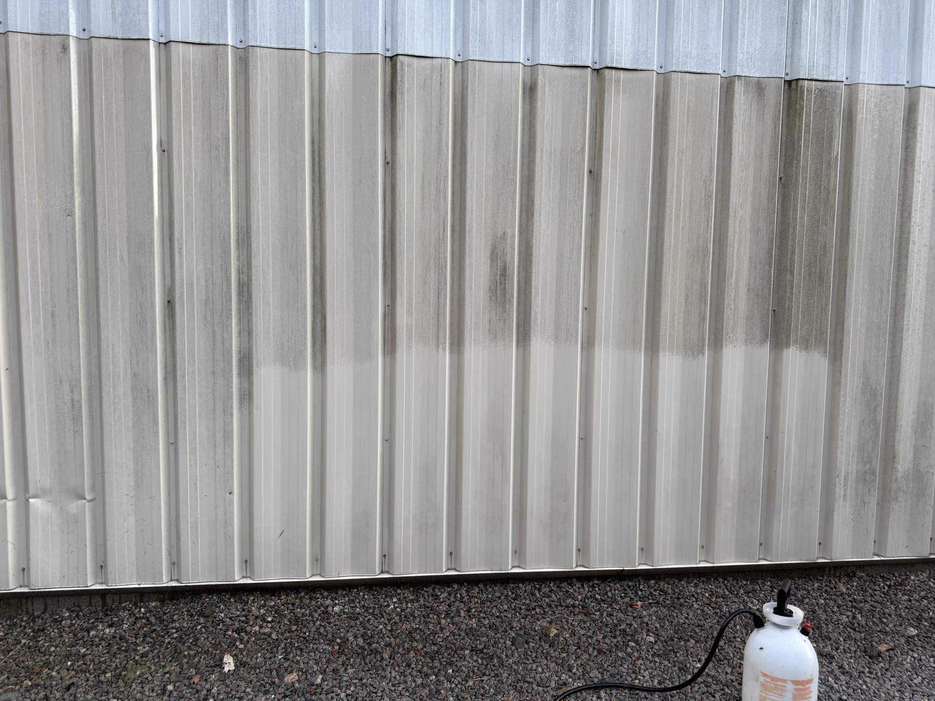 White corrugated metal wall with a small white propane tank on gravel in the lower right corner