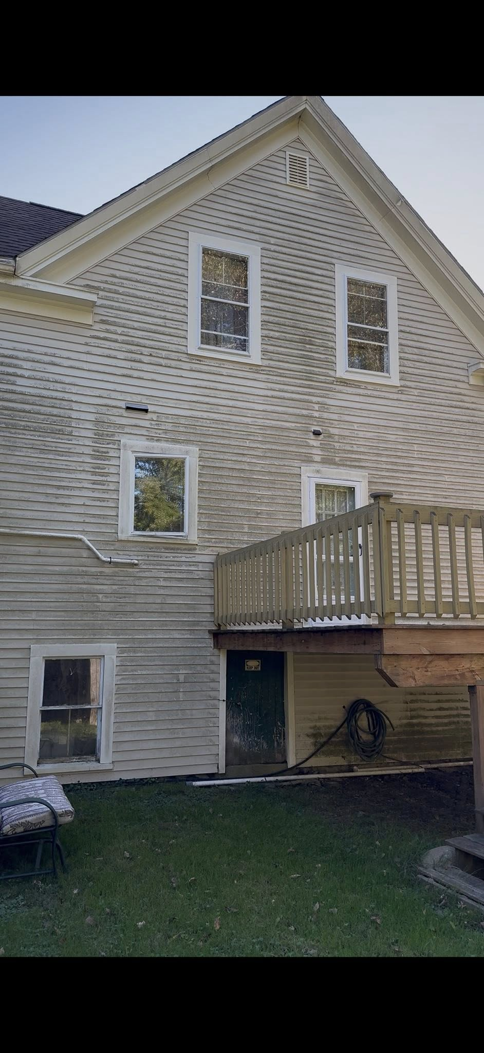Back of a beige house with white trim, small windows, and a wooden deck above a grassy yard