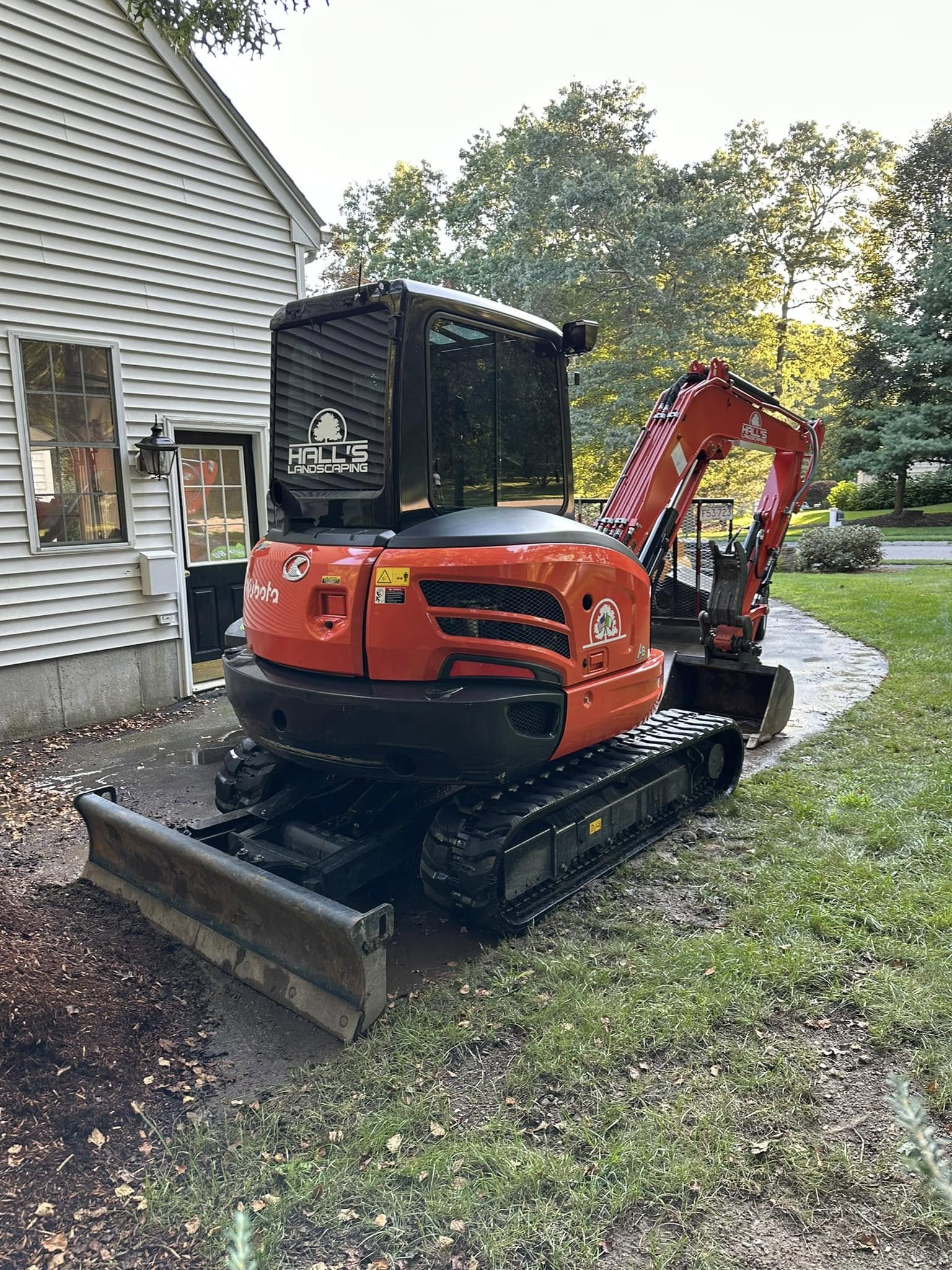 Orange mini excavator beside a house, parked on a gravel driveway with a dirt bucket attached