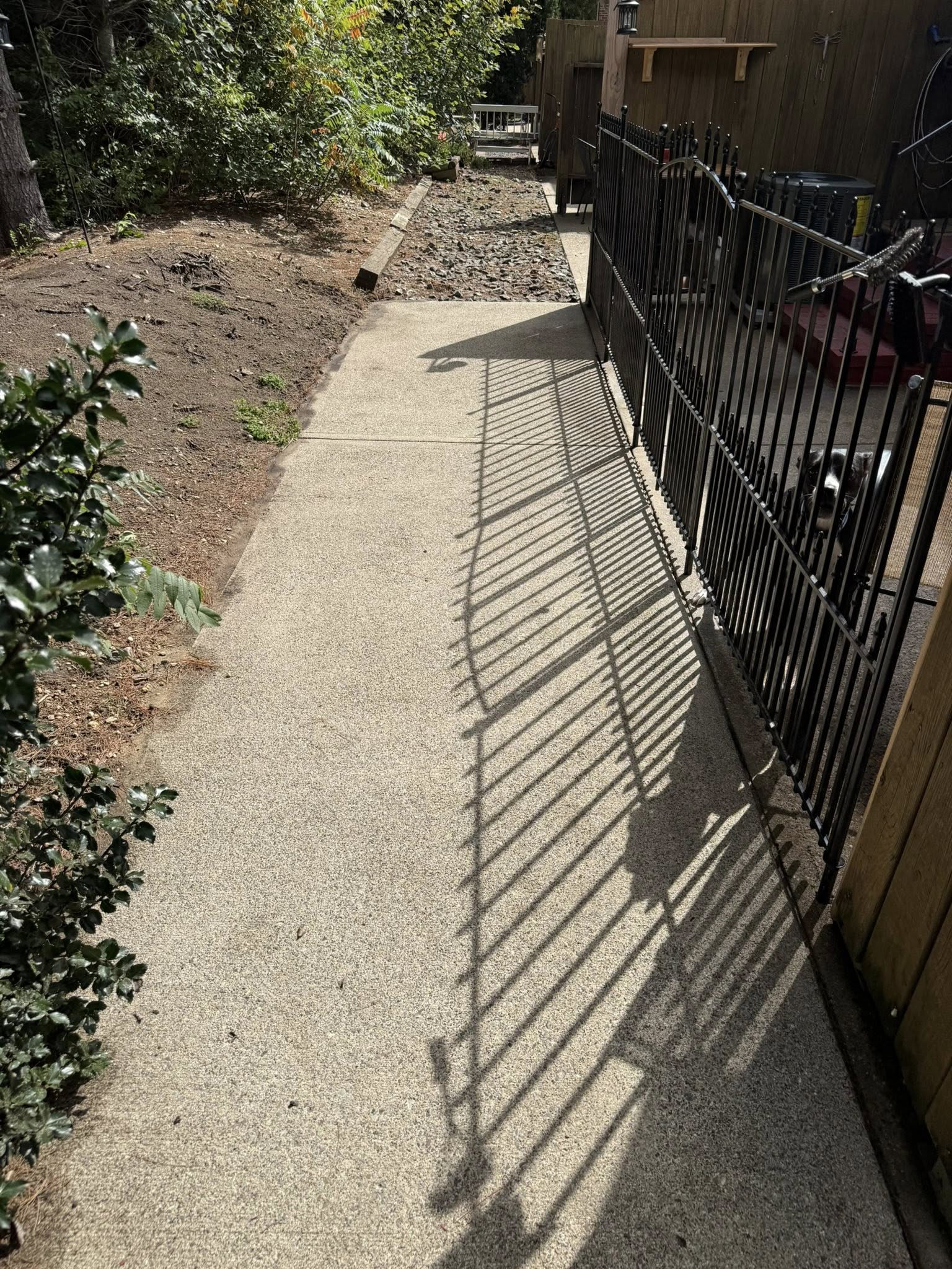 Narrow gravel path beside black metal fence, with sunlight casting striped shadows.