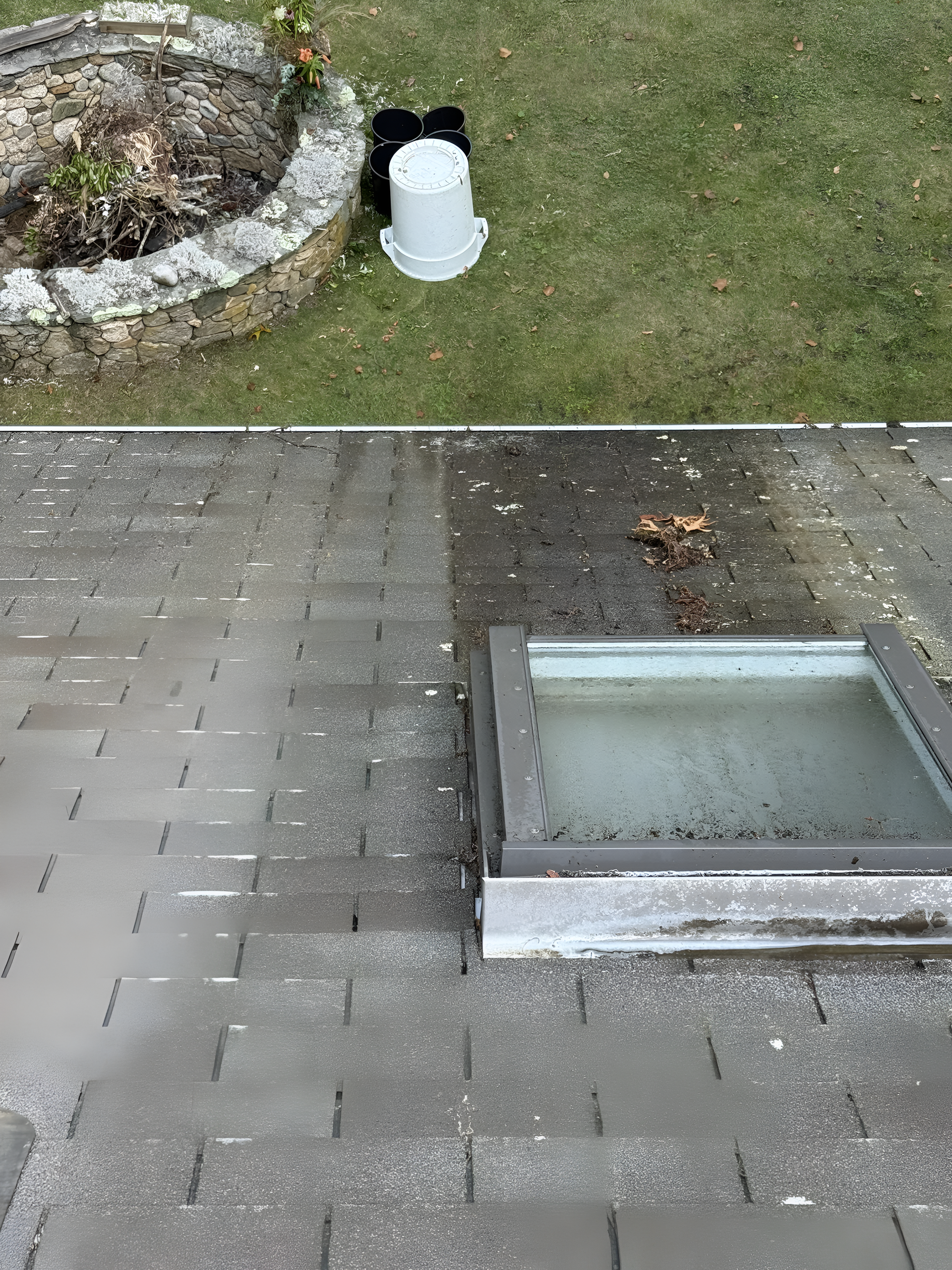 Outdoor paving with a rectangular skylight or basement window beside a grassy edge and stone planter.
