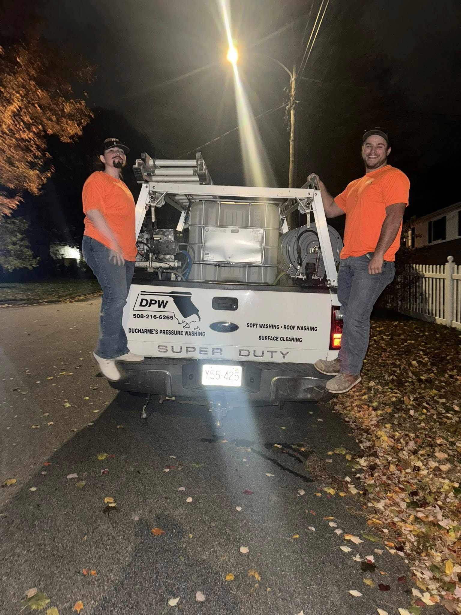 Two workers in orange vests stand by a damaged white utility van on a dark road at night.