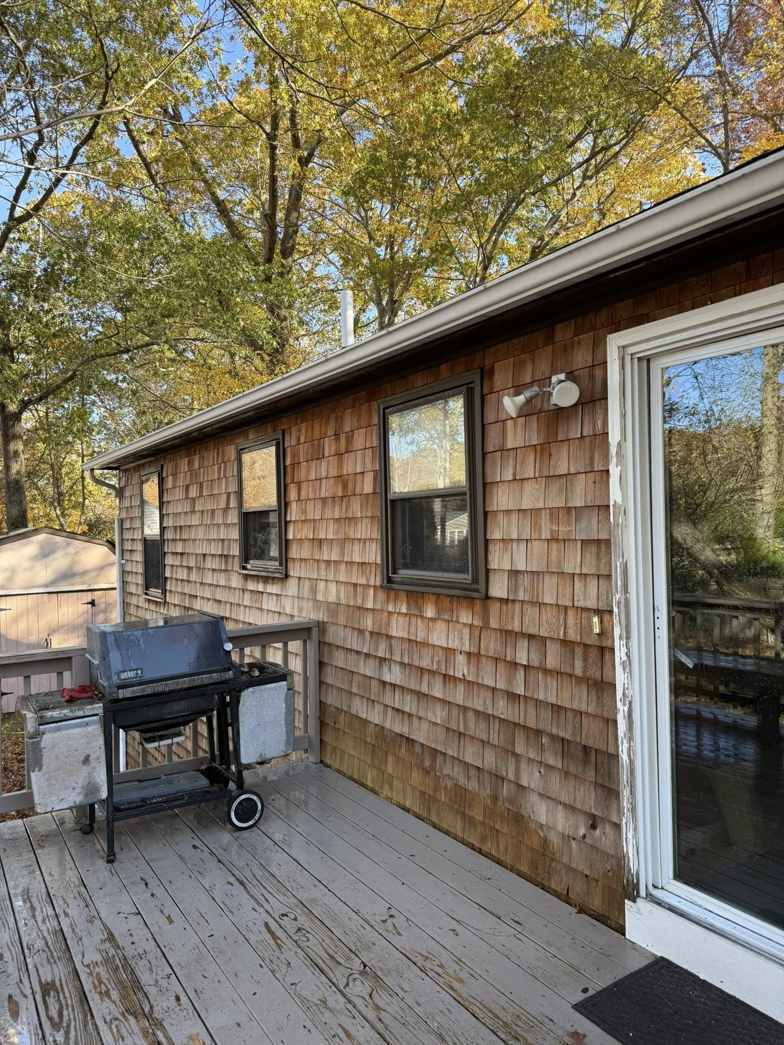 Wood-sided house exterior with deck, grill, and sliding glass door under trees