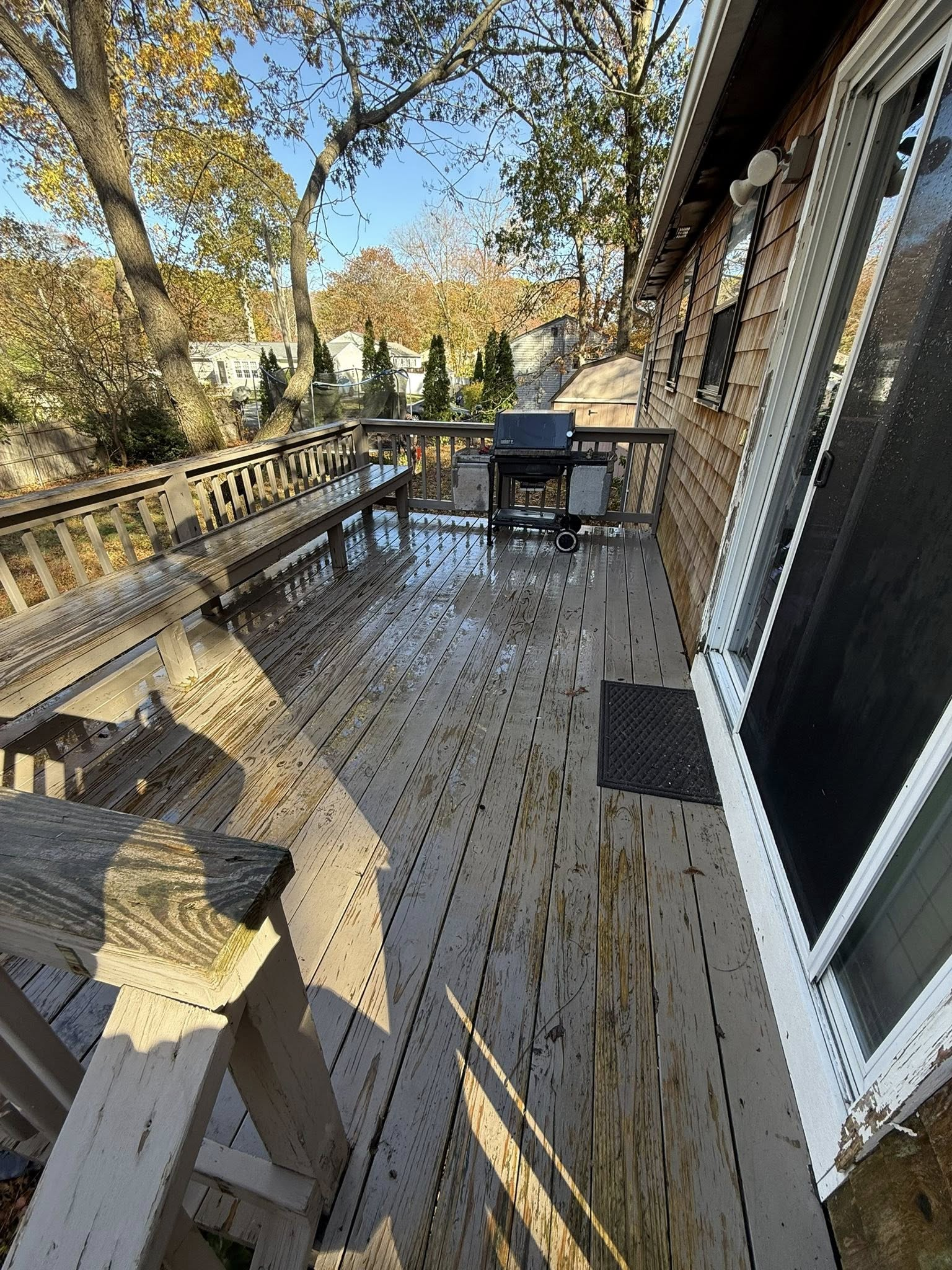 Wooden deck with patio furniture beside a stone house, overlooking trees in autumn sunlight