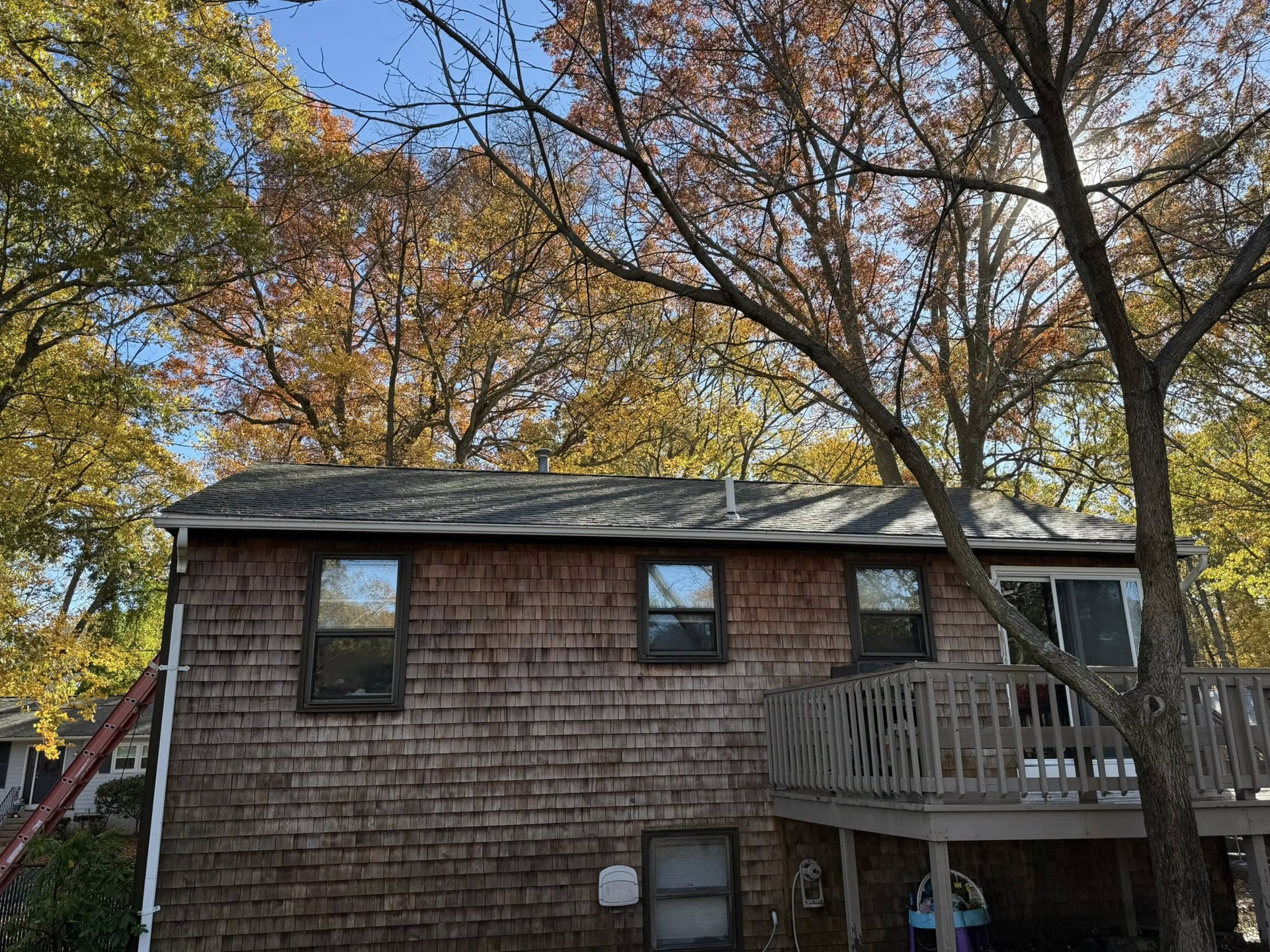 Brown shingled house with a wooden deck and autumn trees overhead