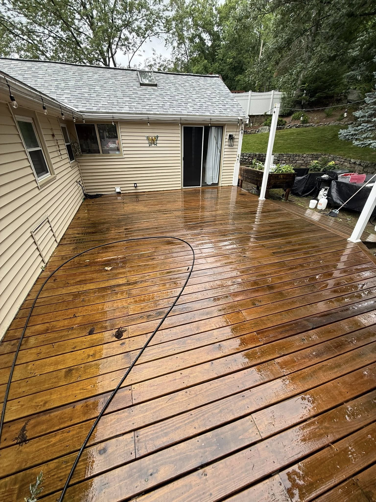 Rainy wooden deck beside beige house with wet leaves and a covered grill area