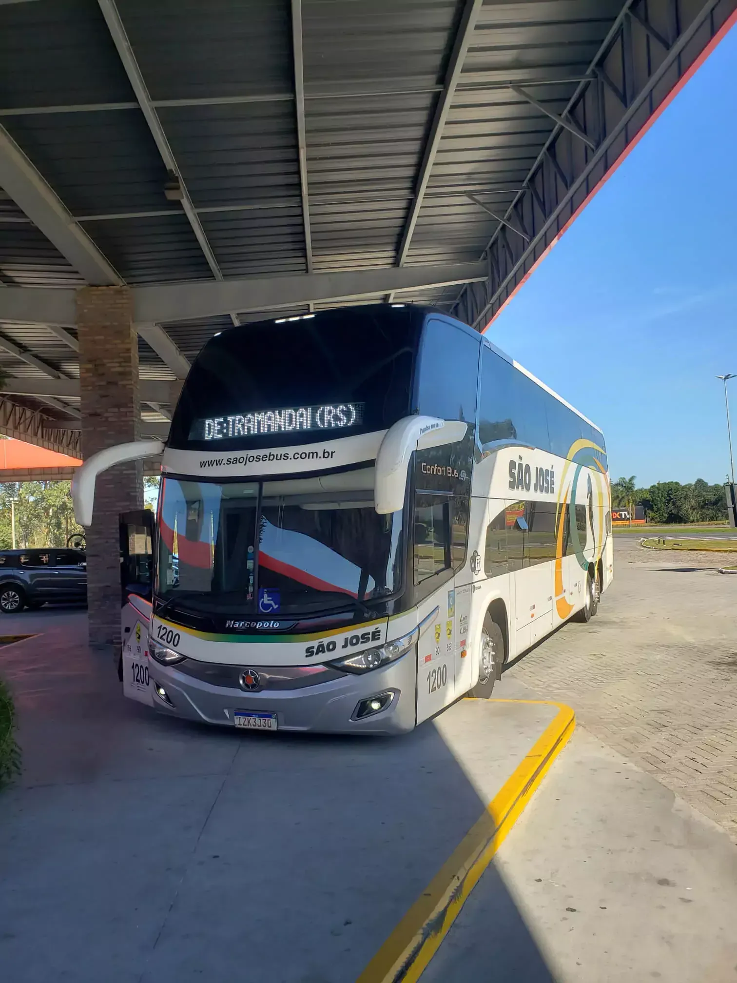 Um ônibus de dois andares da Expresso São José está estacionado sob uma cobertura em uma rodoviária.