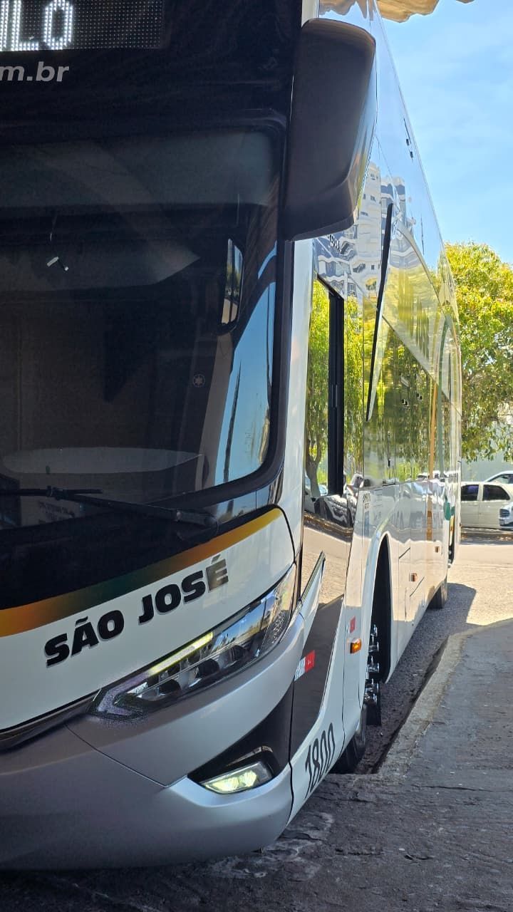 Ônibus urbano cinza estacionado junto ao meio-fio em uma rua ensolarada, com a inscrição “SÃO JOSÉ” visível na frente.