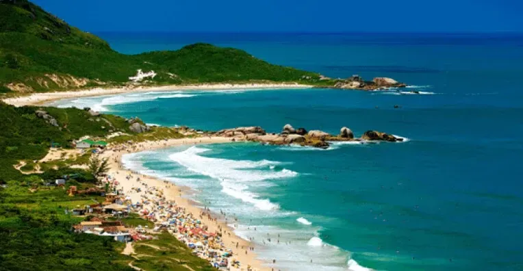 Uma vista aérea de uma praia em Florianópolis com algumas pessoas e ondas chegando