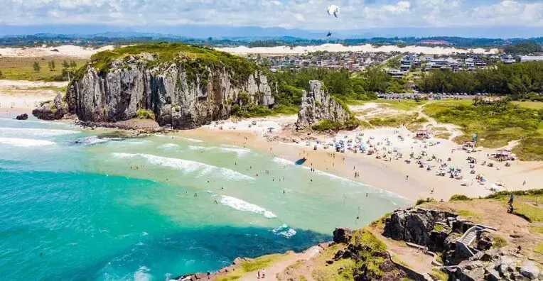 Uma vista aérea de uma praia em Torres no litoral Sul, com uma grande rocha no meio do oceano