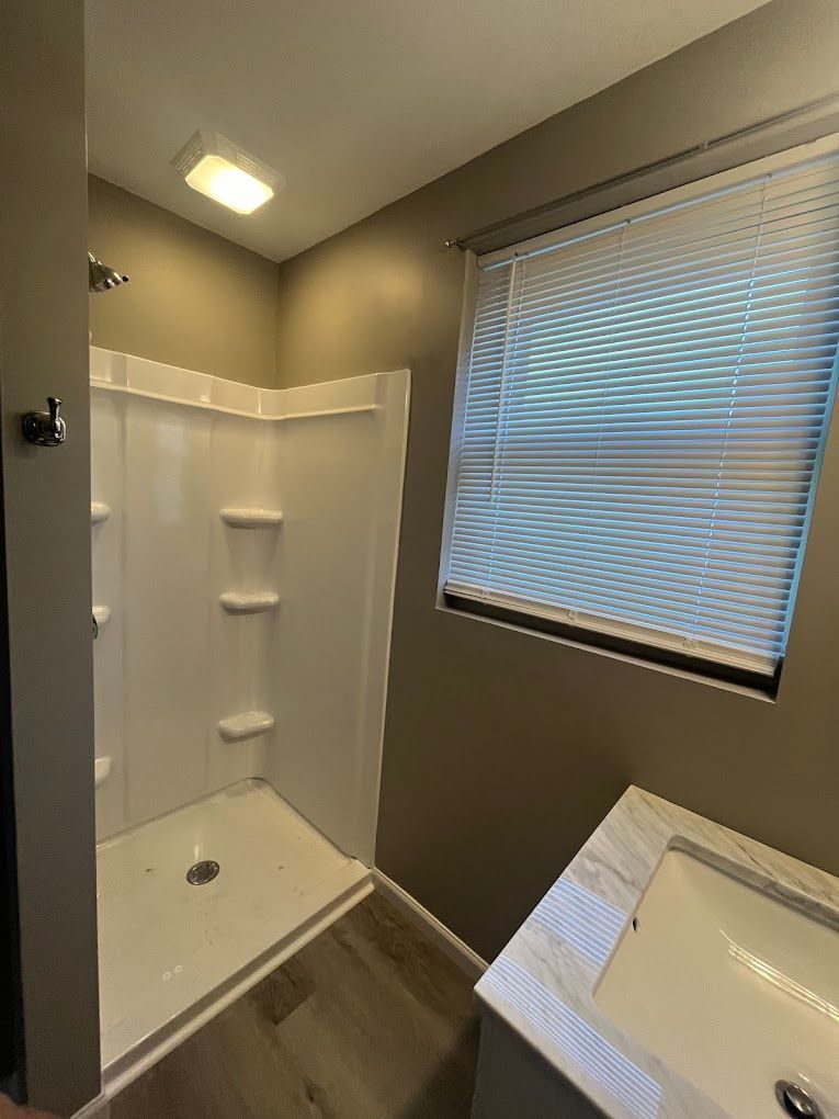 A bathroom with a sink , shower , and window.
