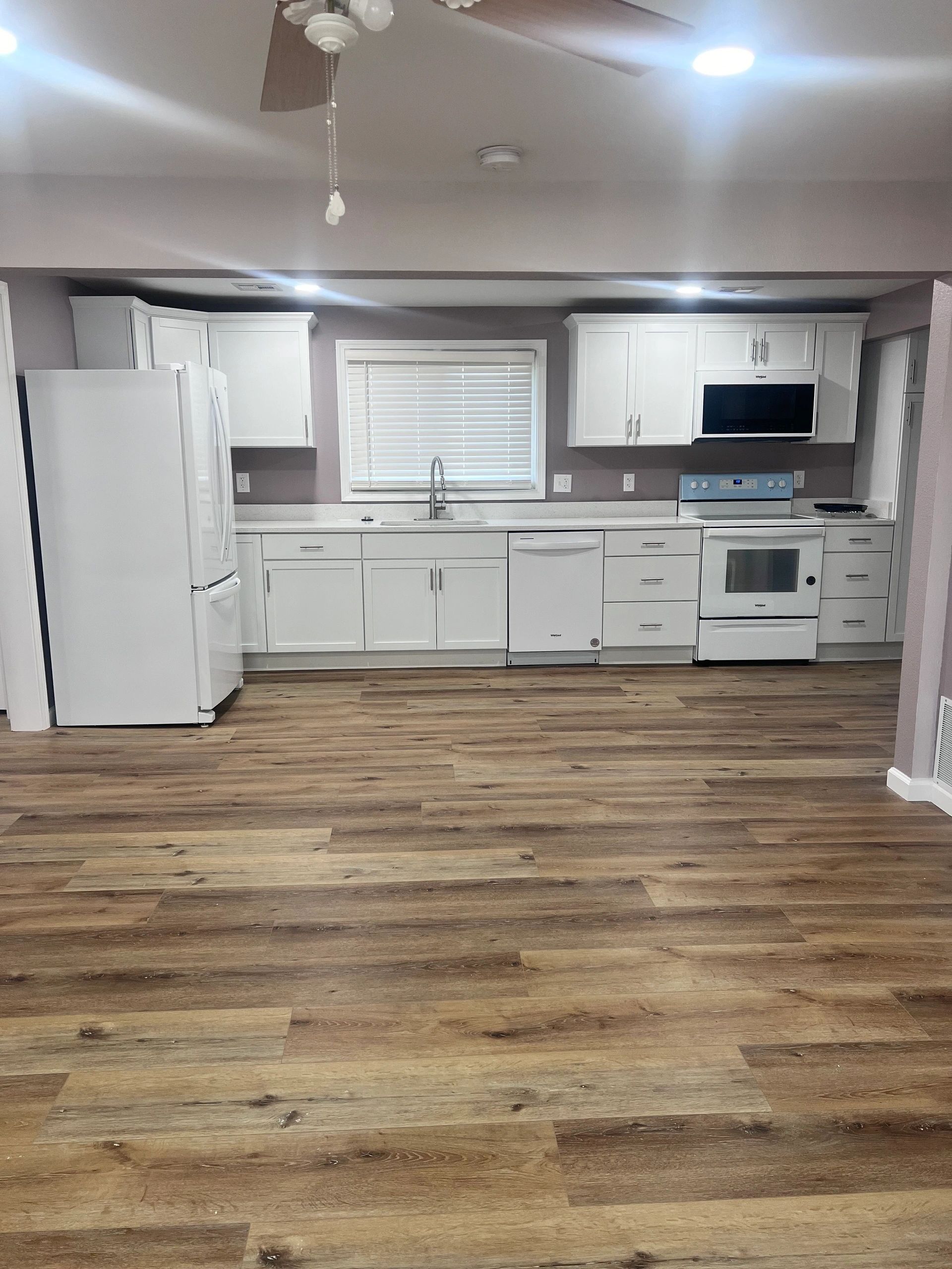 An empty kitchen with hardwood floors and white cabinets