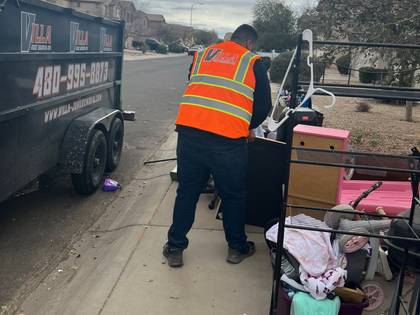 Worker in orange safety vest unloading items from a trailer onto a roadside cart