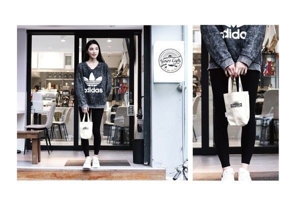 A woman is standing in front of a store holding a tote bag.