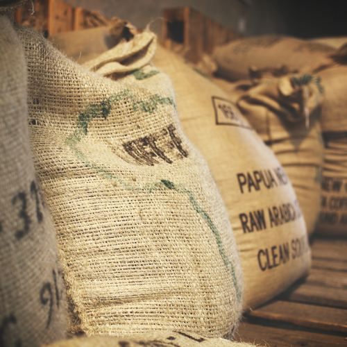 Several bags of papua new guinea raw arabica are lined up on a wooden shelf