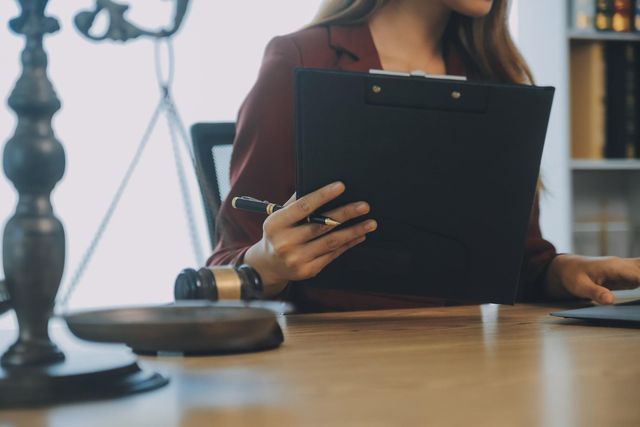 Person holding a clipboard at a desk in a law office with a scale of justice in the foreground