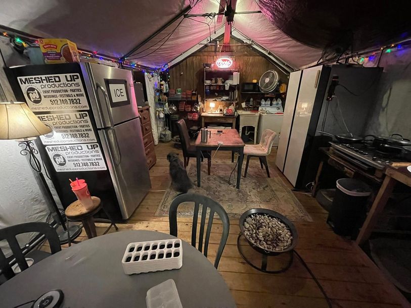 Dimly lit tent interior with chairs, tables, string lights, and a small stove or heater.