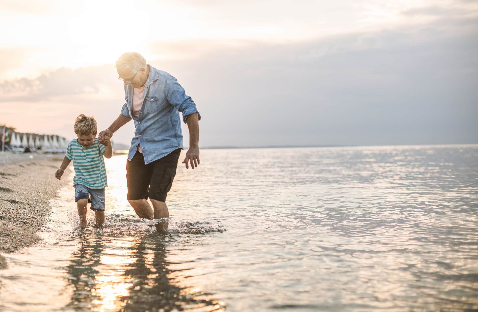 Older man kissing an older woman on the cheek; they are smiling on a beach.