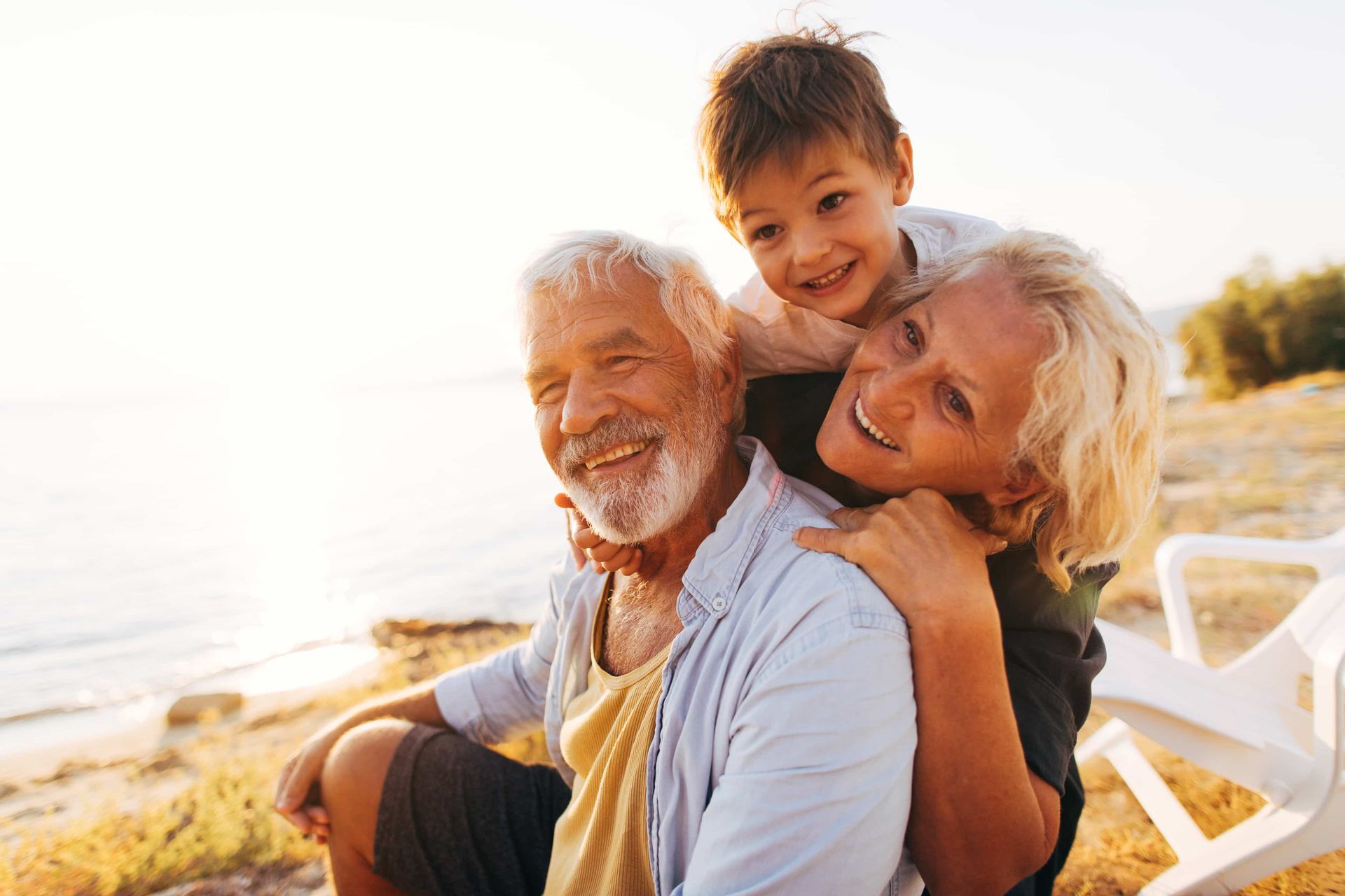 Older man kissing an older woman on the cheek; they are smiling on a beach.