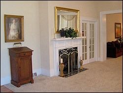 Living room with fireplace, mirror, artwork, and cabinet. Beige walls and carpet.