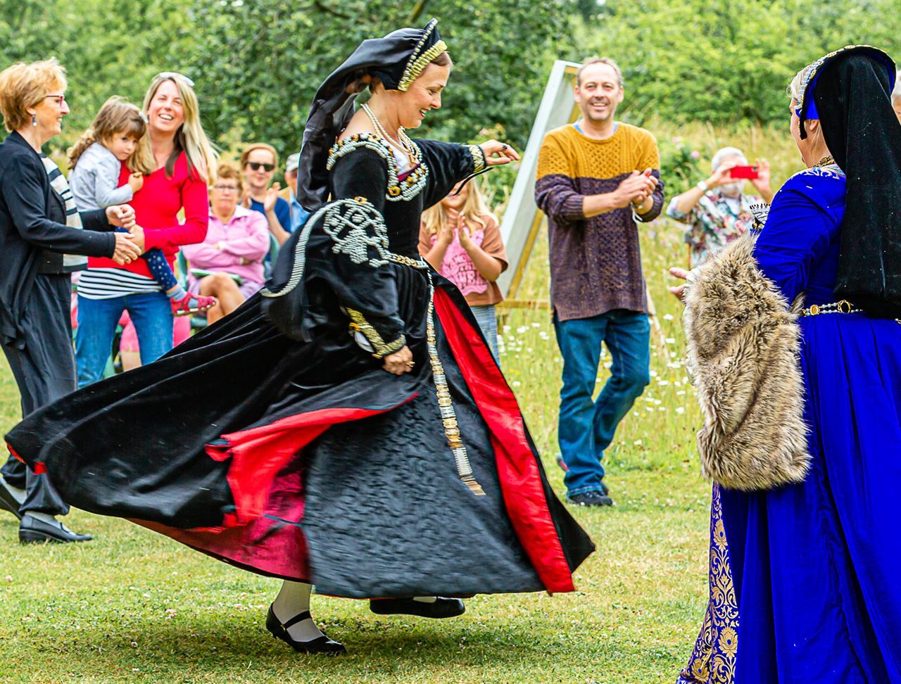 A woman in Tudor dress is dancing in a field.