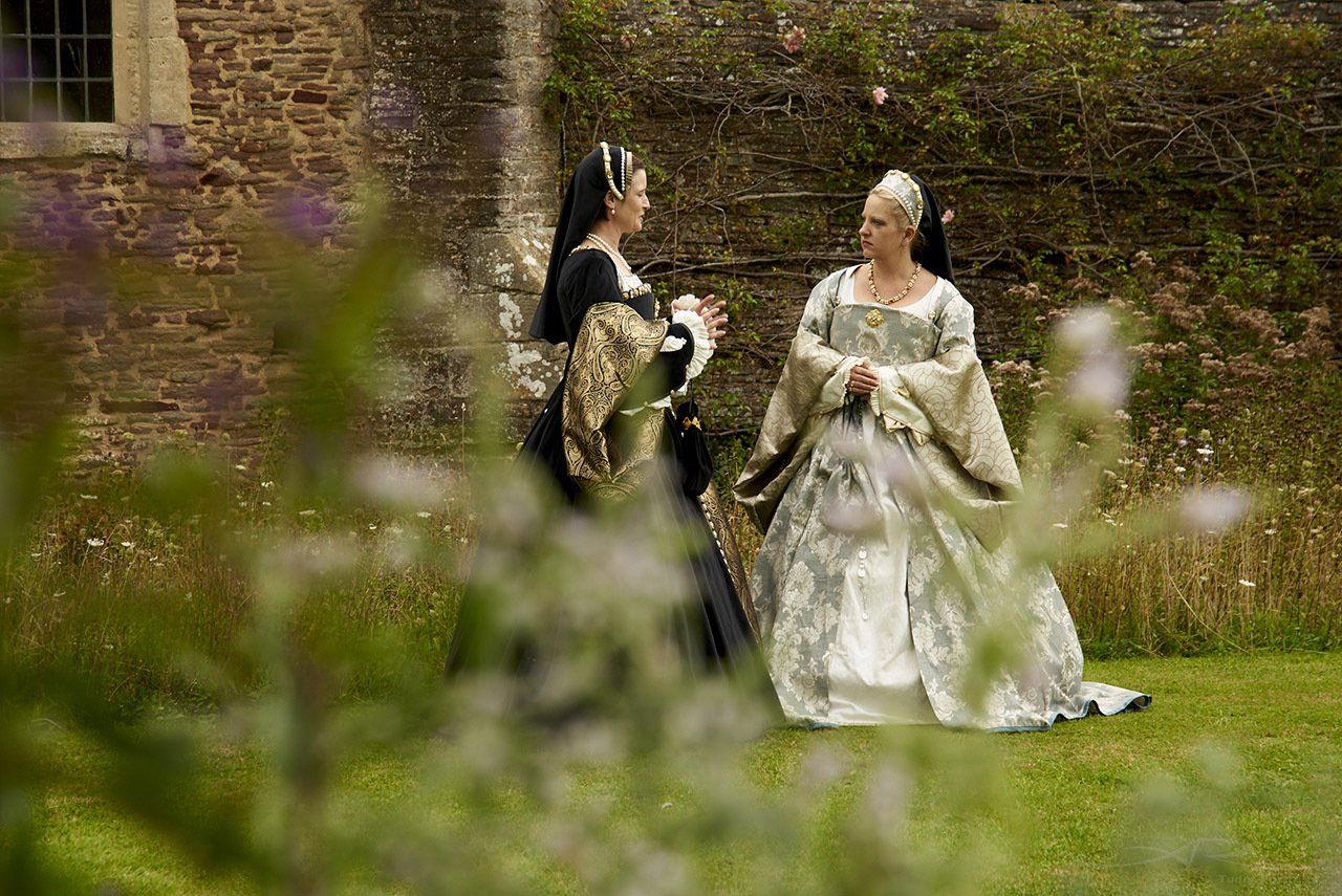 Two women in medieval costumes are standing next to each other in a garden.