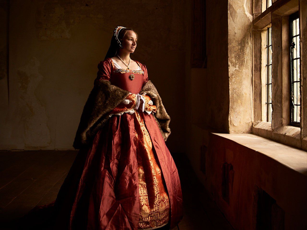 A woman in a red dress is standing in front of a window.