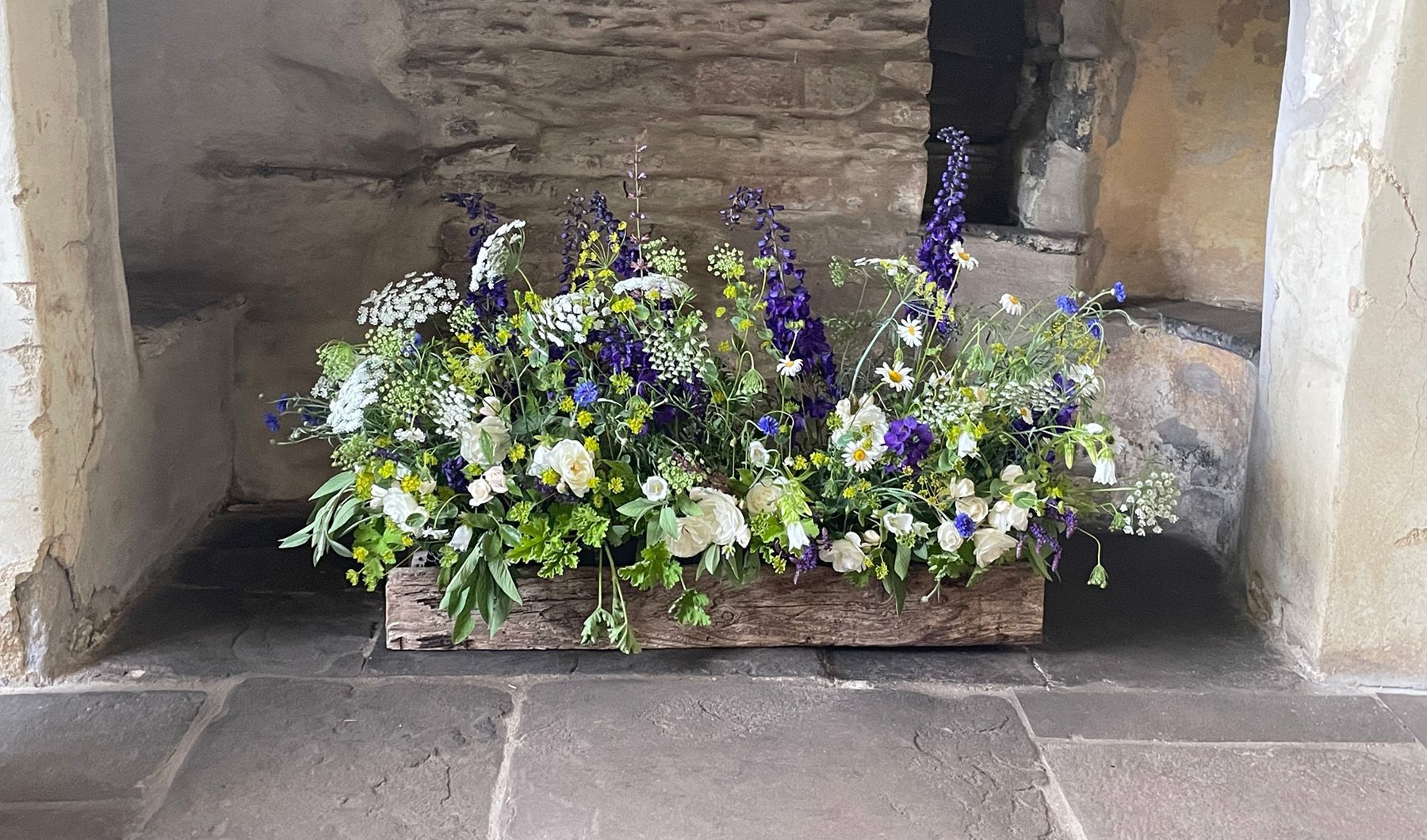 A wooden box filled with flowers is sitting on a stone floor.
