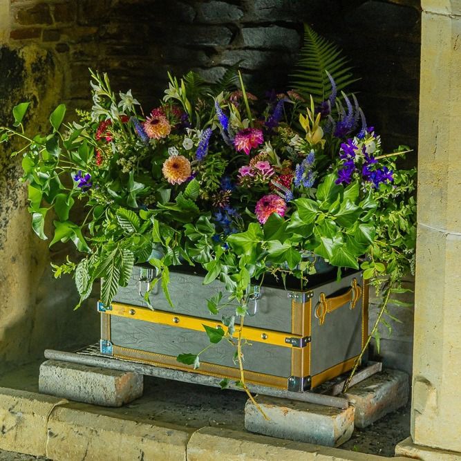 A trunk filled with flowers sits in a fireplace