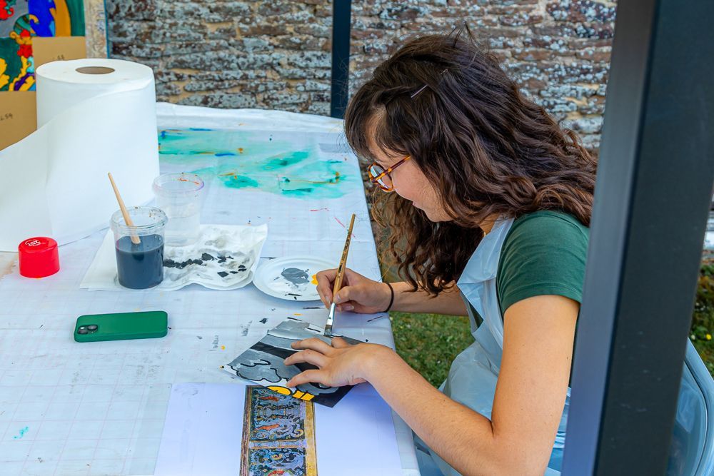 A woman is sitting at a table painting with a brush.