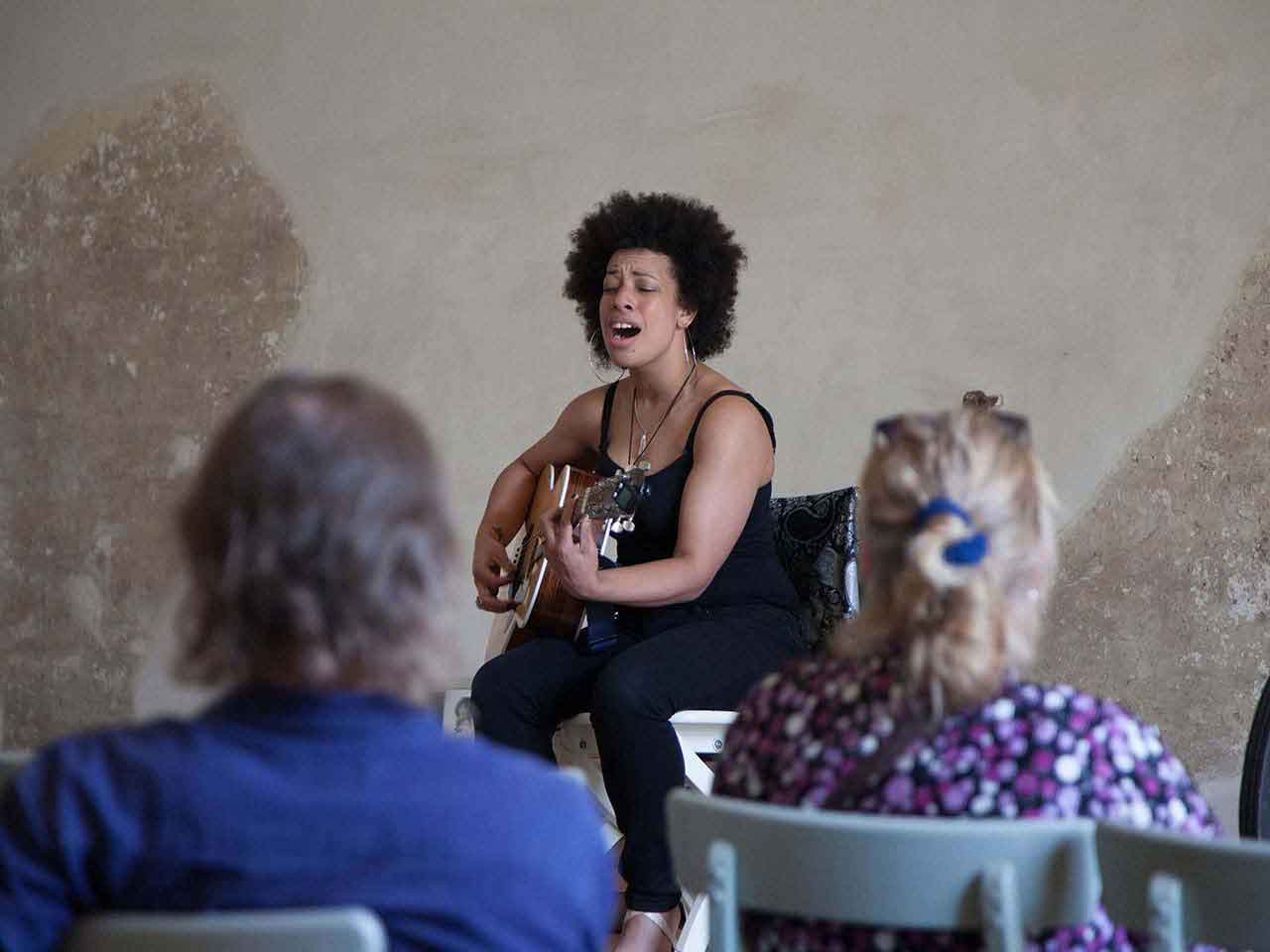 A woman is singing and playing a guitar in front of a group of people.