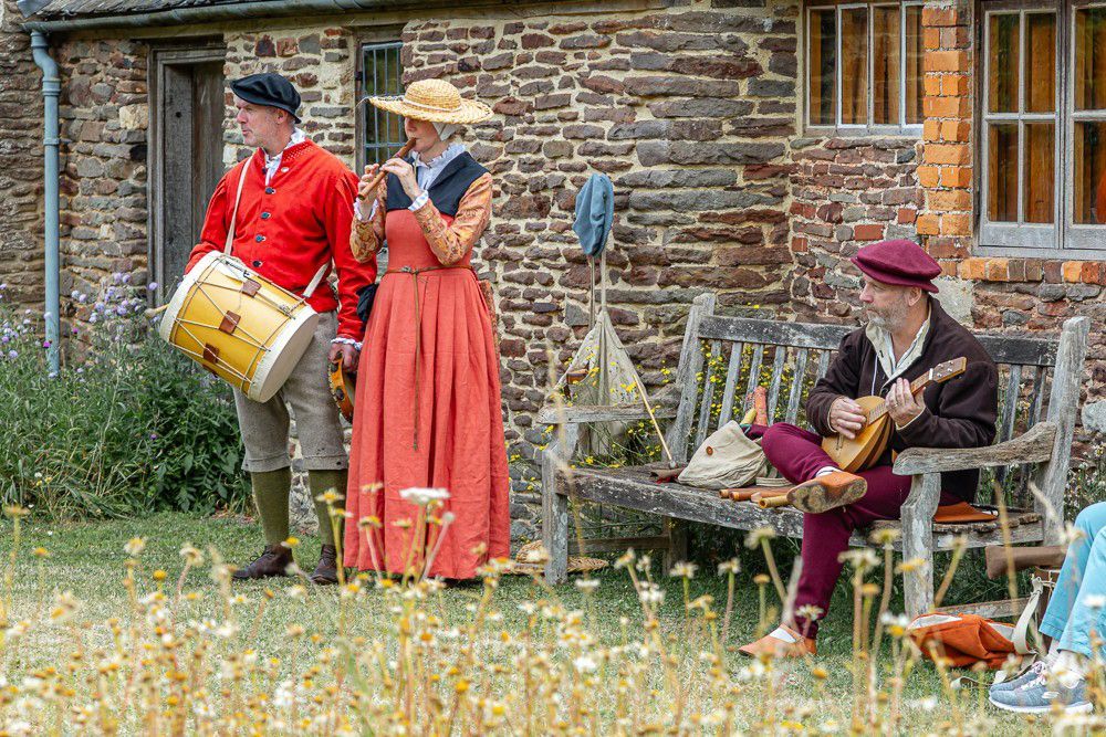 A group of people in medieval costumes are playing instruments in front of a stone building.